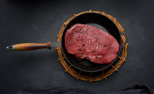 Raw beef tenderloin lies in a metal round frying pan on a black table, top view