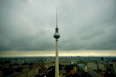 Communications tower in city against cloudy sky