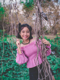 Portrait of smiling girl standing by vines of tree