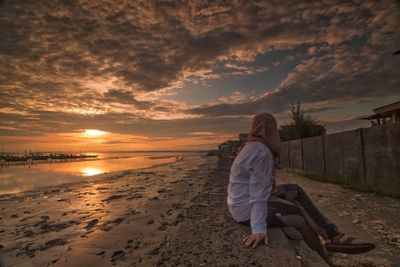 Woman looking at beach against sky during sunset