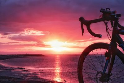 Bicycle by sea against sky during sunset