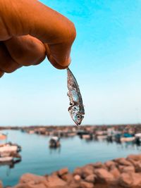 Close-up of hand holding fishing net in sea against sky