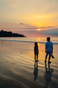 People standing on beach against sky during sunset