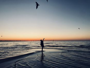 Silhouette woman flying over sea against sky during sunset