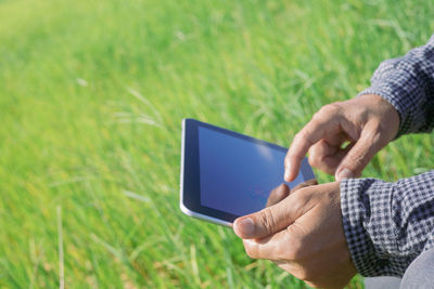 Midsection of man using mobile phone in grass