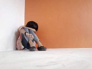 Depressed young woman sitting by wall