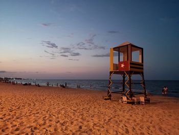 Lifeguard hut on beach against sky during sunset