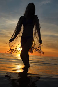Woman standing on beach against sky during sunset