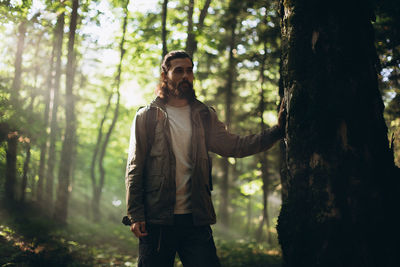 Young man standing by tree trunk in forest