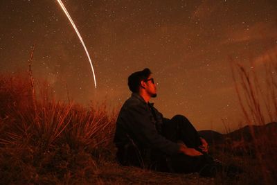 Side view of man sitting against sky at night