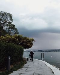 Rear view of person walking on footpath against sea