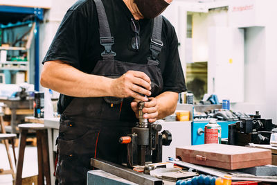 Crop anonymous factory worker wearing uniform working on lathe with drilling machine in contemporary light craftsmanship