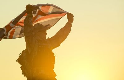 Low angle view of soldier holding british flag against clear sky during sunset