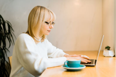 Mature adult woman sitting in cafe with coffee mug and working online on laptop computers 