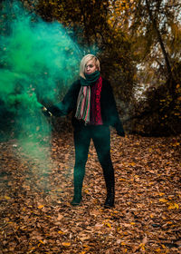 Young woman holding distress flare while standing in forest during autumn
