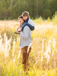 Father carries his son on shoulders. family time outdoors. man with child on autumn field at sunset.