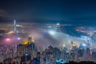 High angle view of illuminated buildings in city at night during foggy weather