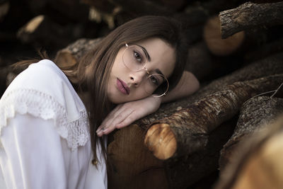 Portrait of a romantic woman with glasses leaning on some wooden logs