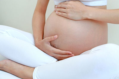 Low section of pregnant woman sitting on bed