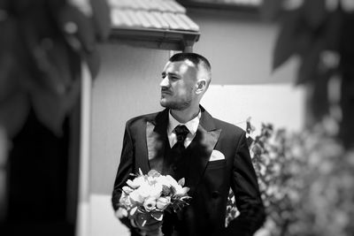 Groom holding bouquet while standing outdoors