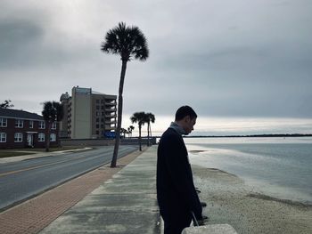 Side view of man standing at beach against sky