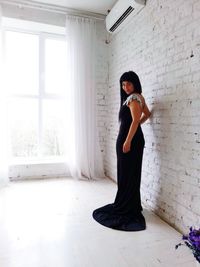 Full length of woman standing by brick wall at home