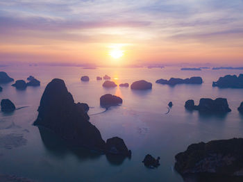 Rocks in sea against sky during sunset