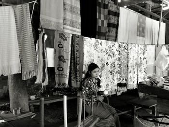 Woman working while sitting by scarves at market