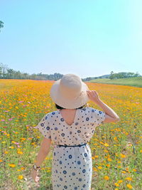 Rear view of woman standing on field by flowering plants against sky