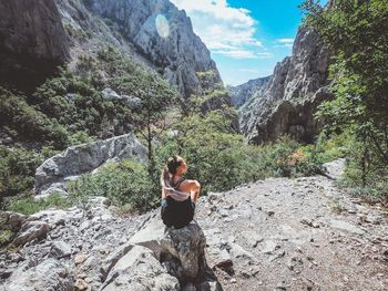 Rear view of young woman sitting on rock against mountain