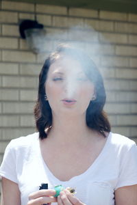 Portrait of young woman holding umbrella against wall