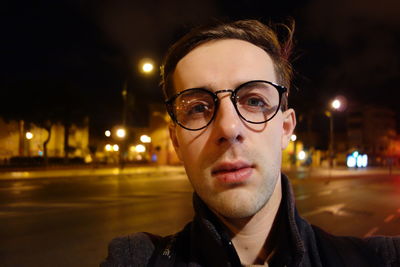 Portrait of man wearing eyeglasses in city at night