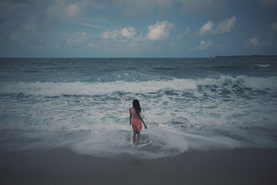 Rear view of woman standing on beach against sky