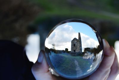 Close-up of hand holding crystal ball against sky