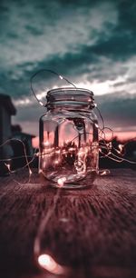 Close-up of glass jar on table against sky during sunset