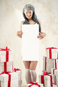 Female model in angel costume holding blank cardboard amidst christmas presents