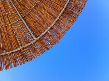 Directly below shot of thatched roof against clear blue sky on sunny day