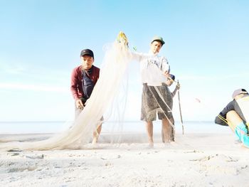 Friends enjoying at beach against sky