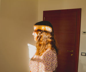 Side view of young woman standing against wall