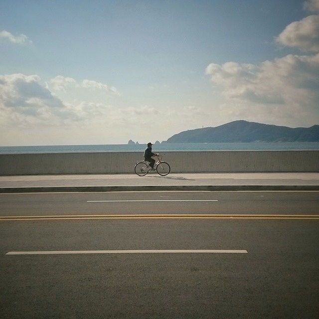 transportation, sky, road, men, full length, cloud - sky, railing, mode of transport, riding, bicycle, lifestyles, land vehicle, cloud, the way forward, sea, leisure activity, rear view, on the move