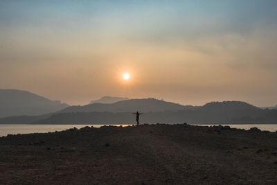 Silhouette person standing on land against sky during sunset