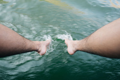 Low section of man touching sea