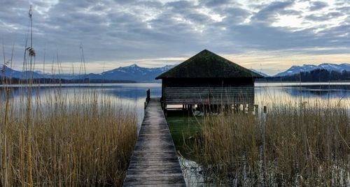 Wooden house by lake against sky