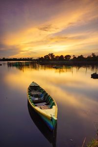 Boat moored in lake against sky during sunset