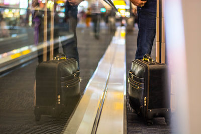 Midsection of man with luggage standing on moving walkway