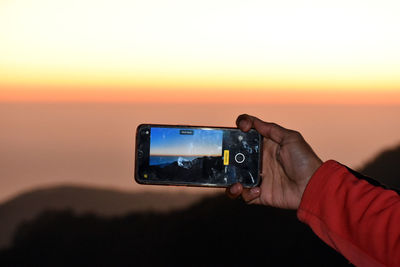 Man photographing on mobile phone at sunset