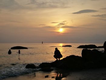 Silhouette rocks on beach against sky during sunset