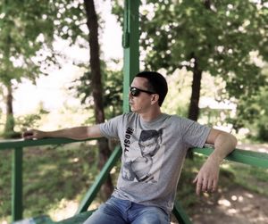 Man wearing sunglasses while sitting against trees