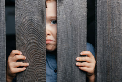 Five- to six-year-old kid in a straw hat peeps through a wooden village fence. copy space