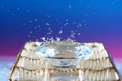 Close-up of water splashing on glass against blue background